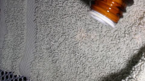 Eine braune Flasche sprüht ein Mittel auf ein handtuch, um Mottenbefall im Haushalt vorzubeugen und abzuschrecken.
