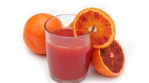 Ein Glas Blutorangengelee ist gefüllt mit frisch gepresstem, leuchtend rotem Saft, umgeben von ganzen und aufgeschnittenen Blutorangen.