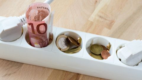Eine Steckdose ist mit einem 10-Euro-Schein und Kleingeld gefüllt, um die hohen Stromkosten im Haushalt zu veranschaulichen.