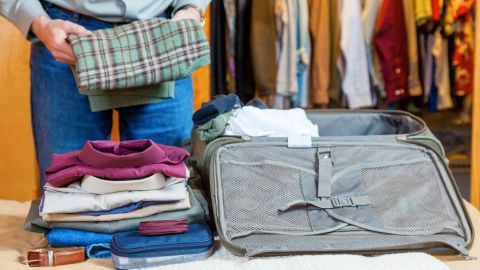 Ein Mann faltet Kleidung und packt sie in einen Koffer, während im Hintergrund ein Kleiderschrank sichtbar ist. Trocknertücher liegen bereit.