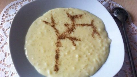 Ein cremiger Milchreis mit Vanillepudding liegt in einer weißen Schüssel, dekoriert mit Zimtfiguren auf einem Tisch.