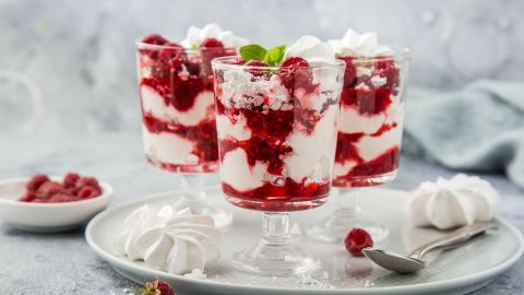 Himbeertraum in Gläsern schichtet Himbeeren, Baiser und Sahne, angerichtet auf einem Teller neben frischen Beeren.