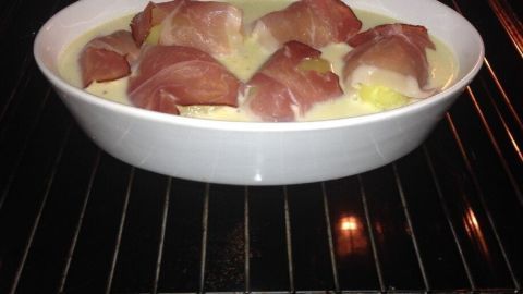 Im Backofen garen Kartoffeln im Baconmantel, umgeben von einer cremigen Zitronen-Sahne-Soße in einer weißen Auflaufform.