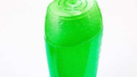 Ein grüner Flakon mit einem offenen Deckel steht vor einem weißen Hintergrund, der mit Fa Magic Oil Duschgel gefüllt ist.