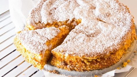 Ein Möhrenkuchen ohne Fett steht auf einem Kuchengitter, leicht angeschnitten und mit Puderzucker bestäubt.
