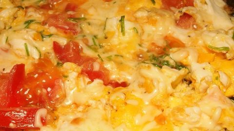 Eine verzierte Pfanne mit Rühreiern, die mit geschmolzenem Käse, Tomaten und Kräutern überbacken sind.