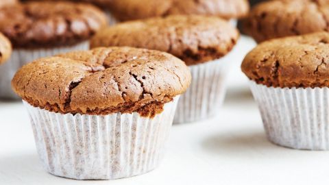 Schokomuffins stehen auf einer Oberfläche und wirken frisch gebacken, umgeben von mehreren ähnlichen Muffins.