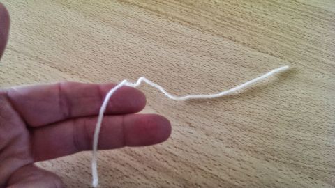 Eine Hand hält einen vergrößerbaren Maschenmarkierer aus Wolle an einem Tisch, bereit zum Einsatz beim Stricken.