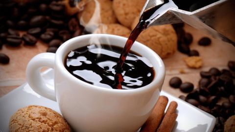 Dampfender Kaffee wird in eine weiße Tasse gegossen, umgeben von Keksen und Kaffeebohnen, die eine gemütliche Atmosphäre schaffen.