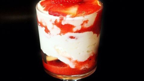 Ein Glas mit Erdbeer Tiramisu zeigt geschichtete Mascarpone-Creme und Erdbeeren, gekrönt von einer frischen Erdbeere.