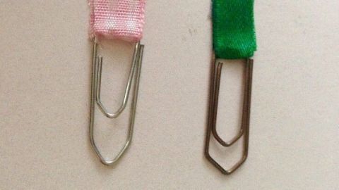 Büroklammern dienen als Lesezeichen, während sie auf einem hellen Hintergrund präsent sind. Pinke und grüne Lesezeichen aus Büroklammern heben sich deutlich hervor.