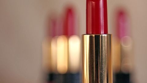 Ein roter Lippenstift steht im Vordergrund, während unscharfe, pinke Lippenstifte im Hintergrund sichtbar sind.