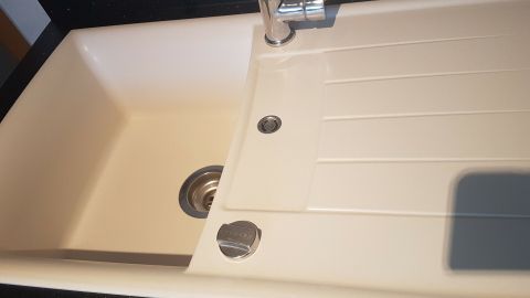 Eine saubere, weiße Spüle steht in einer modernen Küche mit schwarzer Arbeitsplatte, bereit zum Spülen und Reinigen.