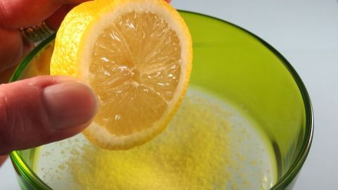 Eine Hand hält eine Zitronenscheibe über ein grünes Glas mit Salz, bereit, es für die Behandlung von Akne und Pickeln zu verwenden.
