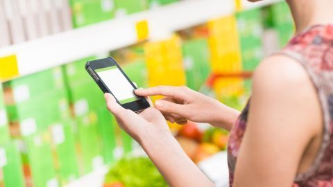 Eine Person hält ein Smartphone und nutzt eine digitale Stempelkarte im Supermarkt zwischen bunten Produktverpackungen.