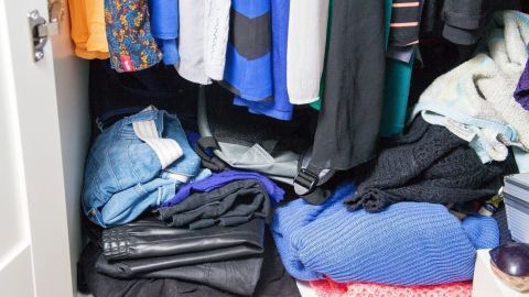 Überfüllter Kleiderschrank mit gestapelter Kleidung, die ungeordnet abgelegt ist und keinen Platz lässt.