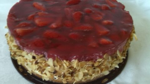 Eine Erdbeertorte mit glasiertem Topping und frischen Erdbeeren, auf einer eleganten Unterlage präsentiert.
