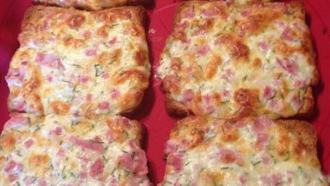 Sechs knusprige Toastscheiben, belegt mit Schinken und einer cremigen Käse-Ei-Mischung, auf einem roten Tablett.