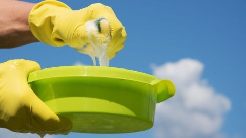 Eine Person mit gelben Handschuhen drückt Seifenblasen aus einer grünen Schüssel in einem blauen Himmel, um schlechte Gerüche im Autositz zu beseitigen.