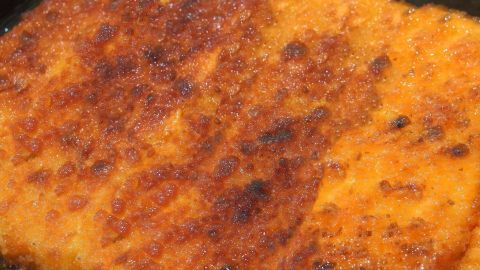 Statt Mehl zum Panieren von Schnitzel, Leber & Co. zu verwenden, kann auch man Stärkemehl nehmen. Knusprige Scheibe mit goldbrauner Panade aus Stärkemehl, frisch aus der Pfanne, umgeben von dunklem Kochgeschirr.
