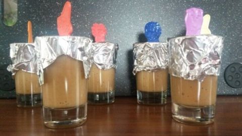 Fünf kleine Gläser mit selbstgemachtem Eis für Kinder, bedeckt mit Alufolie und bunten Löffeln stecken oben drin.