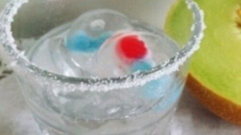 Ein Glas mit XXL Eiswürfeln schimmert in klarem Wasser. Ein grüner Apfel liegt daneben.