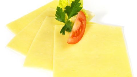 Drei übereinander liegende Käsescheiben liegen zusammen mit einer Scheibe Tomate und frischem Kräutergrün auf einem weißen Hintergrund.