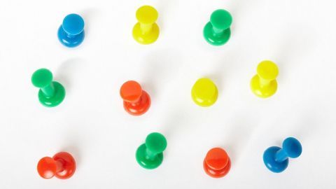 Bunte Reißnägel liegen verstreut auf einer weißen Fläche, bereit zum Befestigen von Notizen an der Wand.