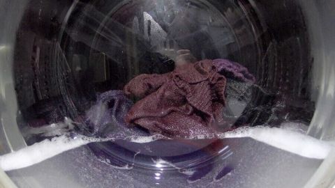 Im Inneren einer Waschmaschine liegt ein lila Kleidungsstück, während Seifenblasen aufsteigen und Wasser sprudelt.