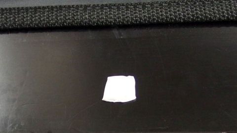 Ein Klebepad liegt auf einer glatten schwarzen Oberfläche und wartet darauf, entfernt zu werden. Der Kontext ist schlicht.