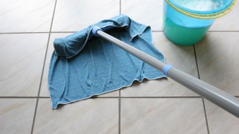 Ein Wischmopp reinigt den Fußboden, während ein Eimer mit Wasser neben ihm steht, in einem klaren Wohnraum.
