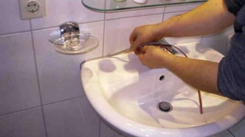 Person erneuert Silikon-Fugen am Waschbecken in einem Badezimmer. Wandfliesen und Pflegeprodukte sind im Hintergrund sichtbar.