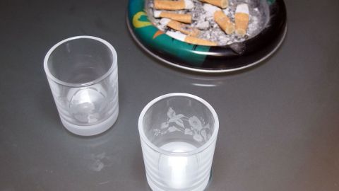 Zwei leere Gläser stehen neben einem Aschenbecher mit Zigarettenresten auf einem Tisch, der für ein Katerfrühstück vorbereitet ist.