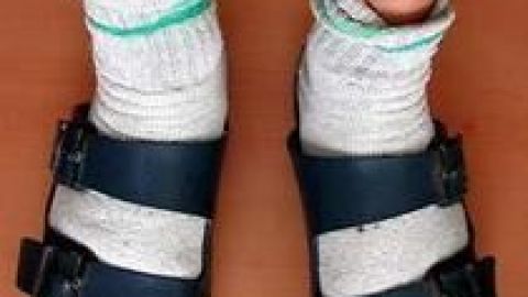 Weiße Socken stecken in offenen Sandalen, während der Träger auf einem Holzfußboden steht. Ein Beispiel für Socken-Stil.