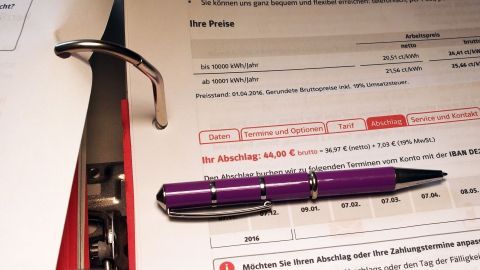 Ein lila Stift liegt auf einem Stapel von Dokumenten, die Abschlagszahlungen für Strom betreffen. Ordnung in einem Ordner.