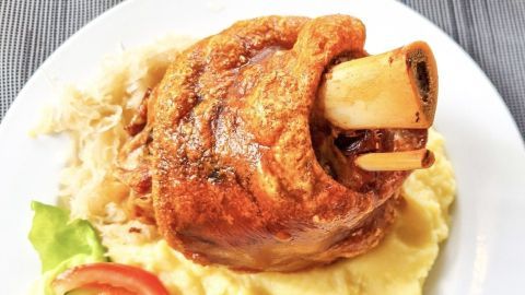 Ein leckerer Schweinshaxe liegt auf cremigem Kartoffelpüree, umgeben von frischem Salat und Tomatenstücken.