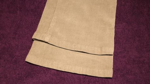 Ein Paar beige Hosenbeine liegt auf einem lila Hintergrund, um die richtige Hosenlänge zu veranschaulichen.