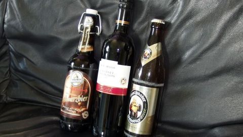Drei Flaschen alkoholischer Getränke stehen nebeneinander auf einer schwarzen Ledercouch. Der Kontext ist entspannt.