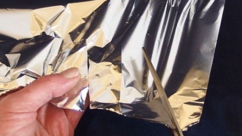 Eine Hand h&auml;lt zerkn&uuml;llte Alufolie, w&auml;hrend eine Schere sie schneidet, um die Sch&auml;rfe zu verbessern.