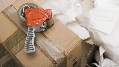 Abroller liegt auf einem zugeklebten Karton, umgeben von zerknülltem Papier, im Kontext von Verpackung und Klebereste.