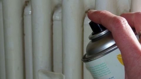 Ein Hand hält eine Sprühdose und sprüht auf einen alten Heizkörper in einem hellen Raum, um ihn wie neu aussehen zu lassen.