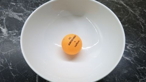 Ein Tablett mit einem eingedellten Tischtennisball liegt in einer weißen Schüssel auf einer dunklen Oberfläche.