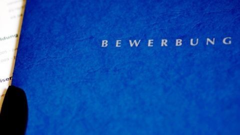 Ein blauer Bewerbungsmappen liegt auf einem Tisch, während sie mit einer Bewerbung und Notizen umgeben ist.