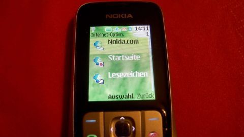Ein Handy zeigt auf dem Bildschirm Menüpunkte während es auf einem roten Untergrund liegt, was schnelles Internet symbolisiert.