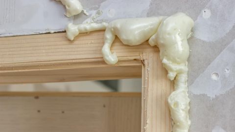 Bauschaum im Haar? Keine Panik, Butter hilft! Wie auf dem Bild sieht Schaum nicht nur an Wänden, sondern auch im Haar aus. Der Artikel erklärt, wie du ihn mit einfachen Mitteln wieder loswirst. Bauschaum verteilt sich um einen hölzernen Türrahmen in einem Raum, während der Untergrund mit Gipsplatten verkleidet ist.