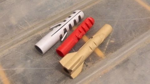 Drei Dübel liegen auf einer Oberfläche, bereit für die Installation in einem Bauprojekt, zeigen verschiedene Formen und Farben.