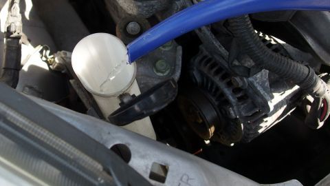 Ein Schlauch führt zu einem Becher, der Wischwasser für das Auto liefert, während der Motorraum geöffnet ist.