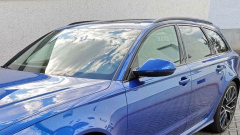 Ein blauer Kombi parkt auf Asphalt; die Autoscheiben spiegeln Wolken, wobei die klare Sicht auf die fortschrittliche Beschichtung hinweist.