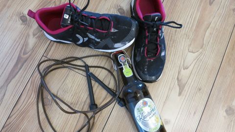 Sportliche Schuhe liegen neben einer Flasche Bier und einem Springseil auf einem Holzfußboden, was einen Kater verdeutlicht.