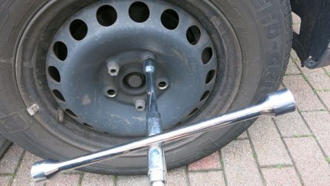 Ich habe mir mein Wagenradkreuz ganz individuell markiert, und zwar derart, dass ich sogar in völliger Dunkelheit oder ähnlichen SOS-Fällen immer genau den einzig richtigen Schraubenschlüssel für mein Auto direkt finde. Ein Rad mit einer schwarzen Felge liegt auf einem Pflastersteinboden, während ein Radmutterschlüssel zum Lösen einer Schraube eingesetzt wird.